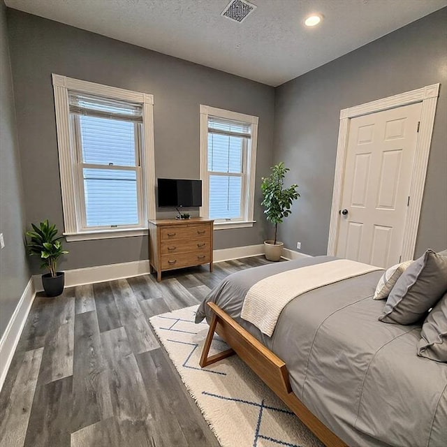 bedroom featuring baseboards, a textured ceiling, visible vents, and wood finished floors