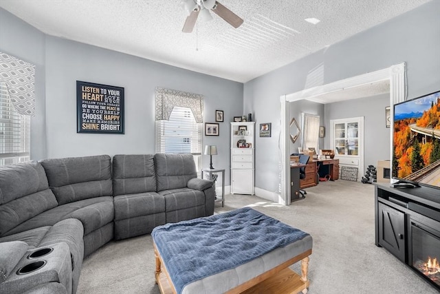 living area with ceiling fan, baseboards, a textured ceiling, and light colored carpet