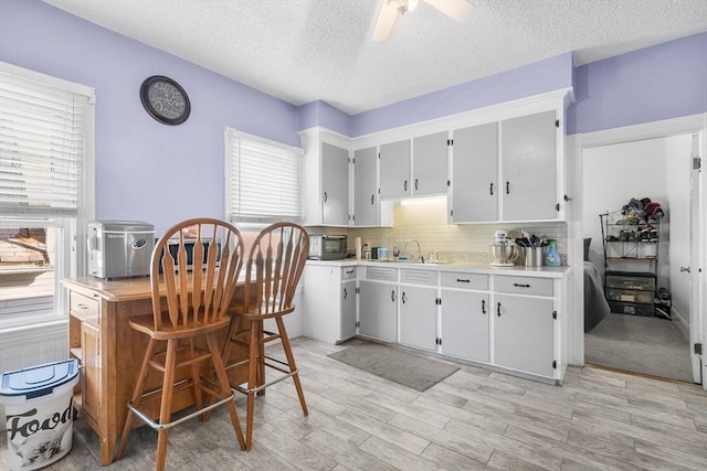 kitchen featuring ceiling fan, a sink, light countertops, light wood-type flooring, and decorative backsplash