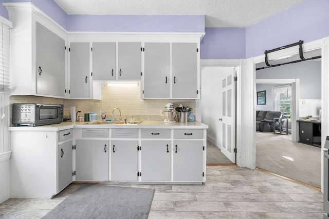 kitchen featuring light countertops, decorative backsplash, light carpet, a sink, and a textured ceiling