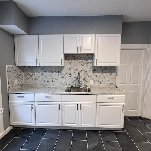 kitchen with dark tile patterned floors, a sink, white cabinetry, light countertops, and decorative backsplash