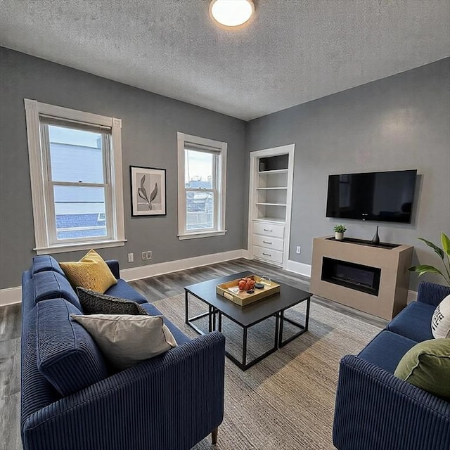 living room featuring baseboards, built in features, wood finished floors, a textured ceiling, and a fireplace