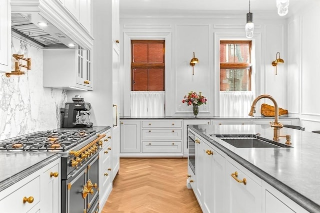 kitchen featuring double oven range, premium range hood, a sink, decorative backsplash, and white cabinetry