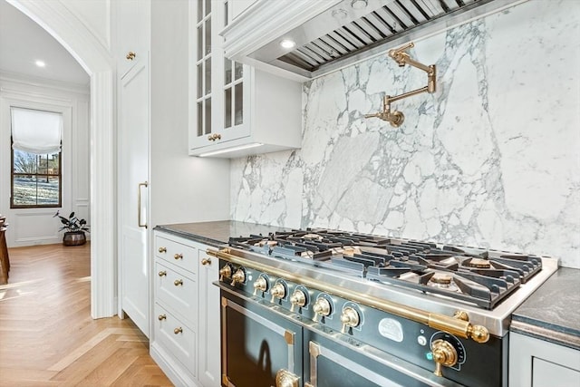 kitchen featuring tasteful backsplash, arched walkways, stainless steel stove, white cabinets, and glass insert cabinets