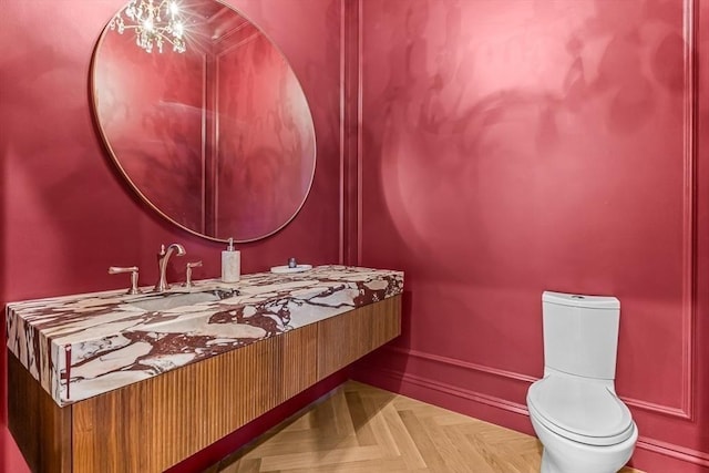 half bath with an inviting chandelier, toilet, vanity, and baseboards