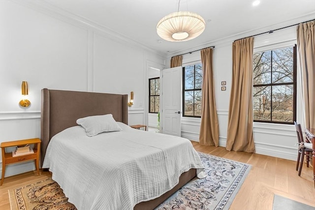 bedroom featuring a decorative wall, light wood-style flooring, and ornamental molding