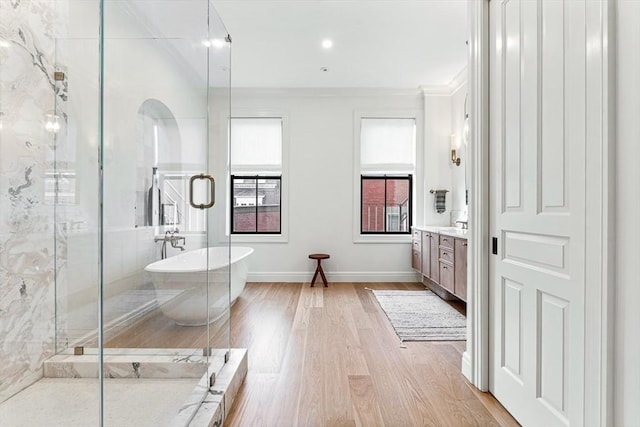 bathroom featuring a stall shower, wood finished floors, crown molding, a soaking tub, and vanity