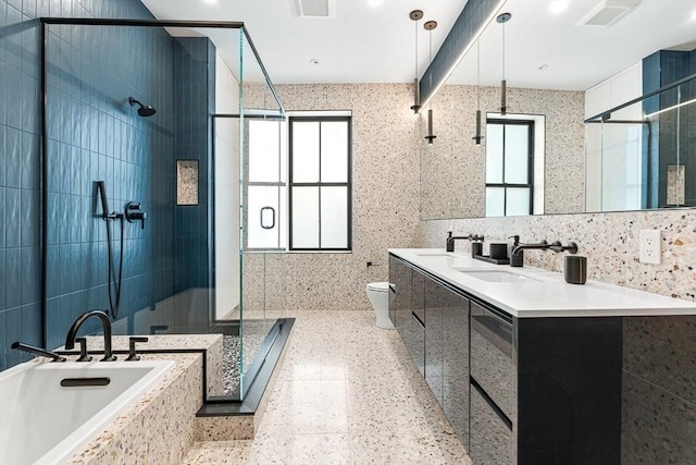 bathroom with a shower stall, toilet, double vanity, a bath, and tile walls