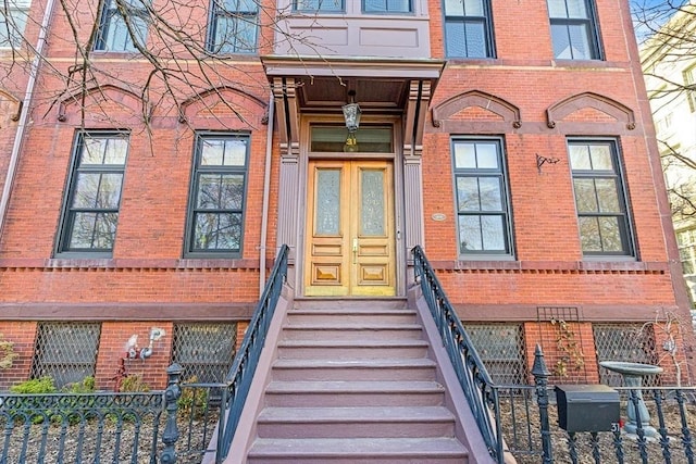 view of exterior entry featuring brick siding and fence