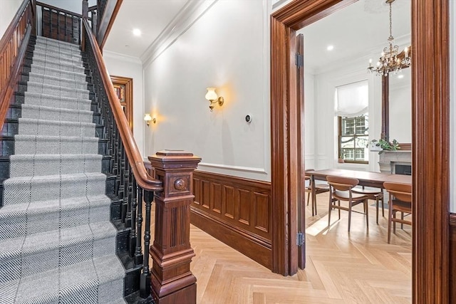 staircase with a decorative wall, a wainscoted wall, ornamental molding, recessed lighting, and a notable chandelier