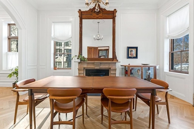 dining area featuring ornamental molding, arched walkways, an inviting chandelier, a fireplace, and a decorative wall