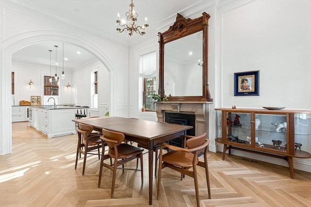 dining space with crown molding, a fireplace, an inviting chandelier, arched walkways, and a decorative wall