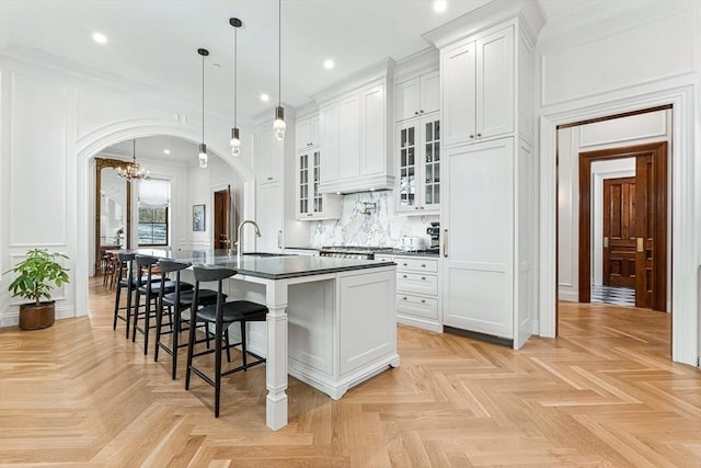 kitchen with arched walkways, a large island with sink, a kitchen bar, dark countertops, and a decorative wall