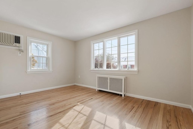 spare room featuring radiator, light hardwood / wood-style flooring, and a wall unit AC