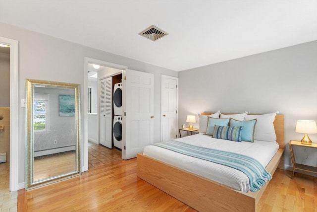 64 Prospect St Unit B, Marblehead, MA 01945 - bedroom with stacked washing machine and dryer, a baseboard radiator, and light wood finished floors