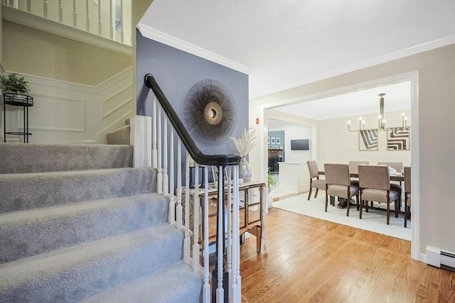 stairway featuring hardwood / wood-style flooring, ornamental molding, an inviting chandelier, and a baseboard heating unit