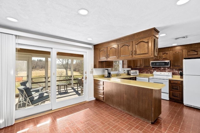 kitchen with tasteful backsplash, white appliances, kitchen peninsula, and a textured ceiling