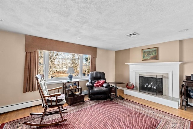 living area with a baseboard radiator, a tiled fireplace, hardwood / wood-style floors, and a textured ceiling