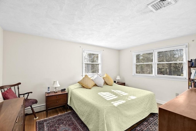 bedroom featuring a baseboard heating unit, a textured ceiling, and dark hardwood / wood-style floors