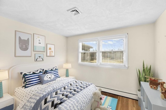 bedroom with a baseboard heating unit, wood-type flooring, and a textured ceiling