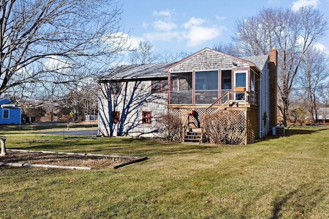 rear view of house featuring central air condition unit, a sunroom, and a lawn