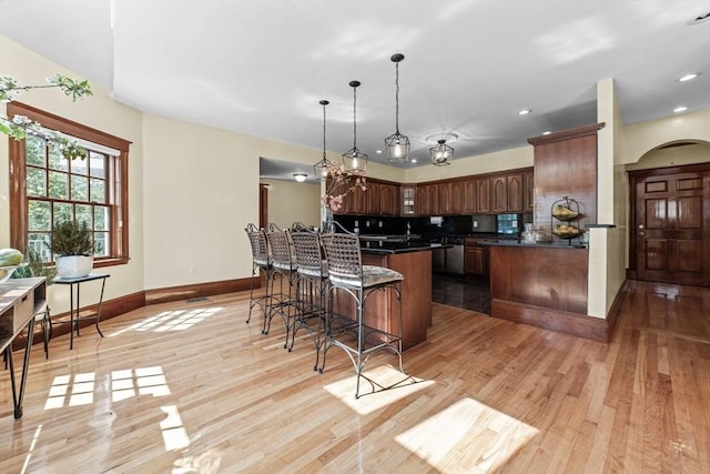 72 Charlemont St, Newton, MA 02461 - kitchen with dark countertops, a kitchen breakfast bar, baseboards, arched walkways, and light wood-style flooring