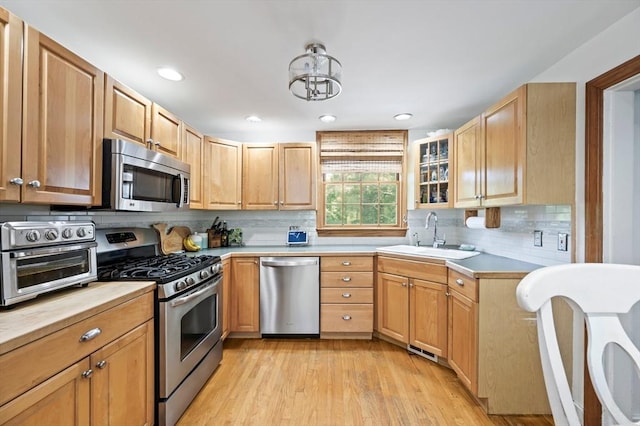 89 W Elm St, Pembroke, MA 02359 - kitchen featuring appliances with stainless steel finishes, decorative backsplash, light wood-style flooring, glass insert cabinets, and recessed lighting