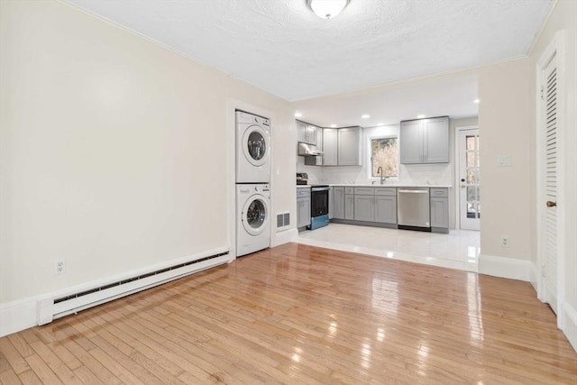 washroom featuring stacked washing maching and dryer, sink, a baseboard heating unit, a textured ceiling, and light hardwood / wood-style flooring