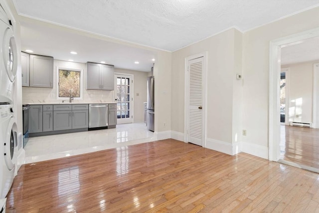 kitchen with sink, gray cabinets, appliances with stainless steel finishes, stacked washer and clothes dryer, and light wood-type flooring