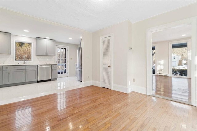 unfurnished living room featuring a baseboard heating unit, sink, and light wood-type flooring