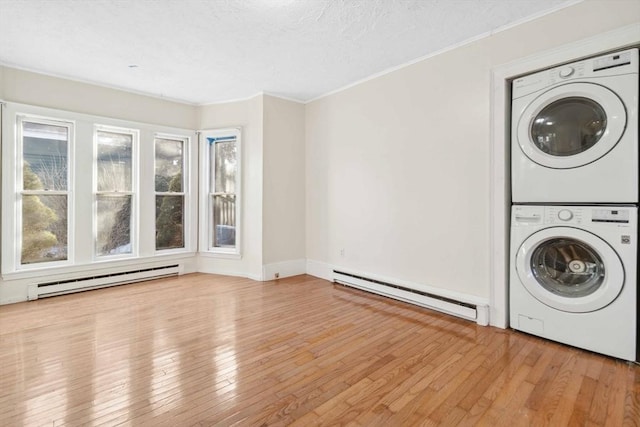 laundry area featuring baseboard heating, stacked washing maching and dryer, crown molding, and light wood-type flooring