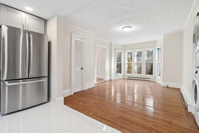 kitchen with ornamental molding, stainless steel fridge, stacked washer / dryer, light hardwood / wood-style floors, and a baseboard heating unit