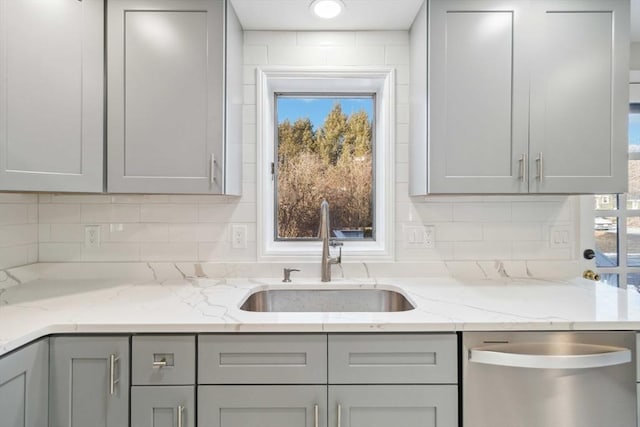 kitchen featuring stainless steel dishwasher, gray cabinets, sink, and light stone countertops