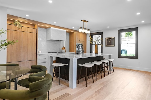 kitchen with a large island with sink, a breakfast bar area, light stone countertops, decorative light fixtures, and light wood-type flooring