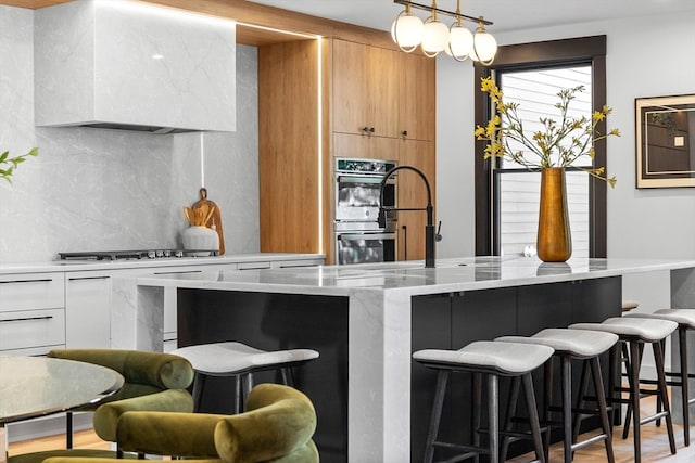 kitchen with white cabinets, exhaust hood, light stone counters, light hardwood / wood-style flooring, and decorative light fixtures