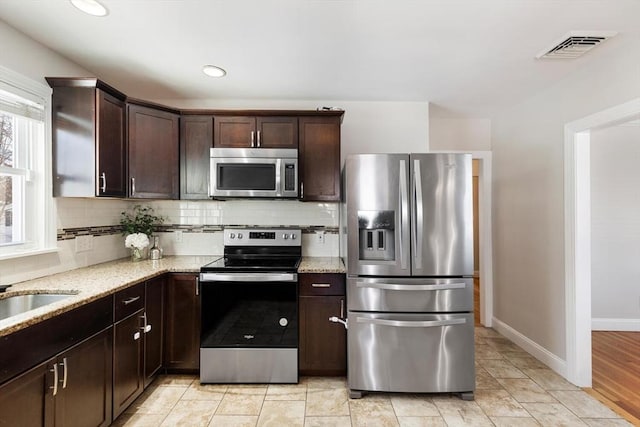 kitchen featuring dark brown cabinetry, stainless steel appliances, backsplash, and light stone countertops