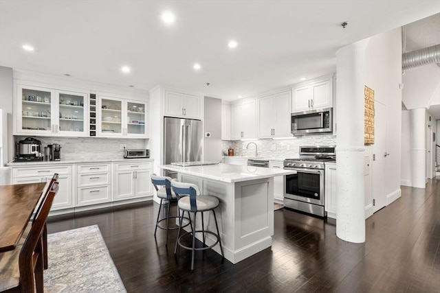 kitchen with appliances with stainless steel finishes, dark wood-type flooring, decorative backsplash, a center island, and white cabinetry