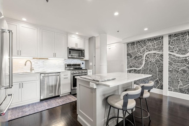 kitchen with white cabinets, stainless steel appliances, a kitchen island, and dark wood-type flooring