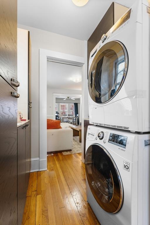 laundry room featuring ceiling fan, stacked washing maching and dryer, and light hardwood / wood-style flooring