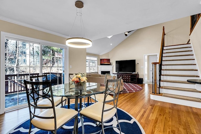 dining space with lofted ceiling, a fireplace, wood finished floors, ornamental molding, and stairway