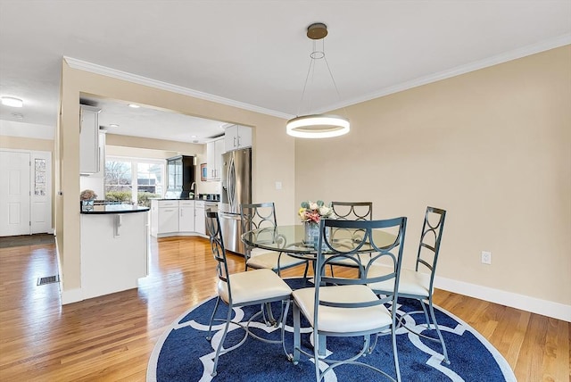 dining area featuring baseboards, light wood finished floors, visible vents, and crown molding