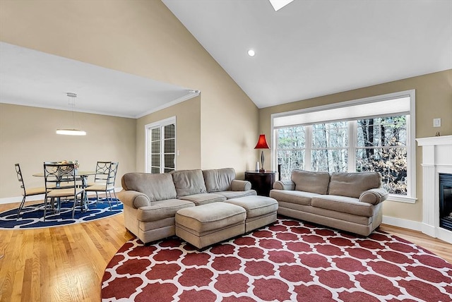 living area with crown molding, baseboards, wood finished floors, and a glass covered fireplace