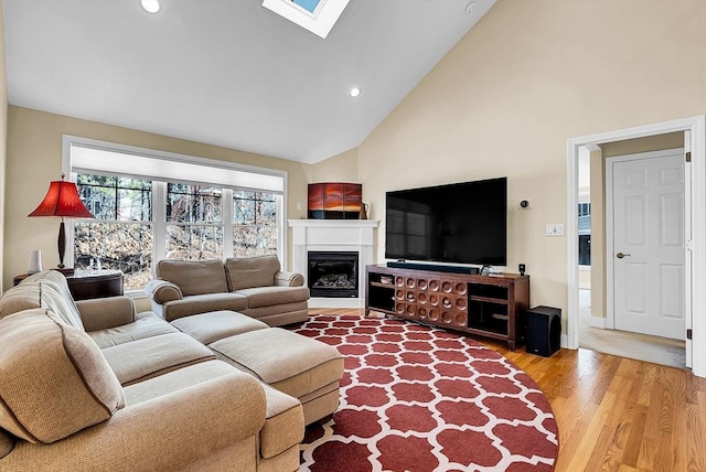 living area with high vaulted ceiling, recessed lighting, a skylight, wood finished floors, and a glass covered fireplace