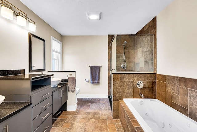 bathroom with stone tile floors, toilet, a shower stall, vanity, and a whirlpool tub