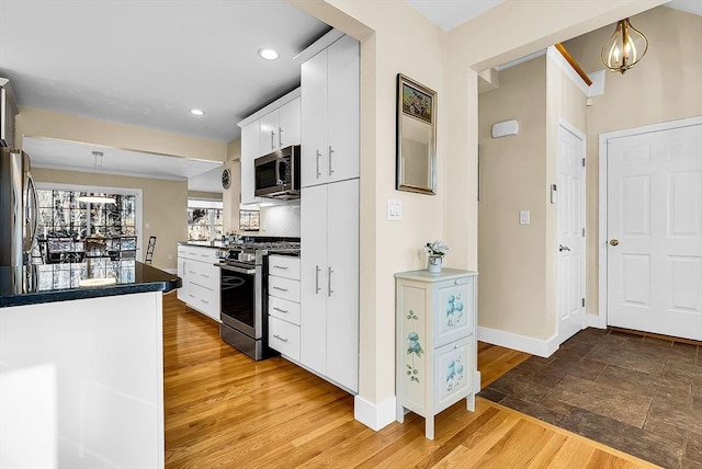 kitchen with light wood finished floors, white cabinets, dark countertops, decorative light fixtures, and stainless steel appliances