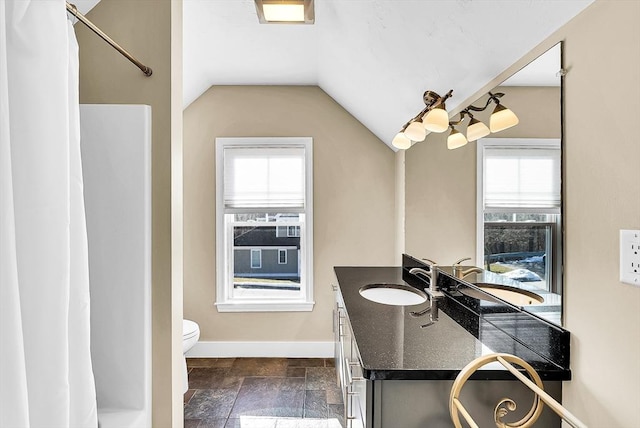 bathroom with baseboards, lofted ceiling, toilet, stone tile flooring, and vanity