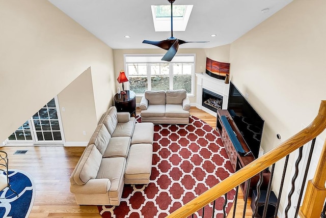 living room featuring a skylight, baseboards, a ceiling fan, wood finished floors, and a fireplace