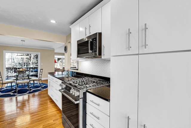 kitchen with white cabinets, appliances with stainless steel finishes, light wood finished floors, dark countertops, and tasteful backsplash