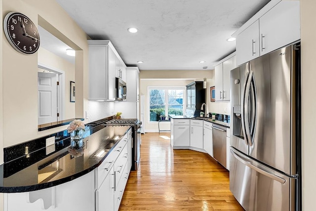 kitchen with a peninsula, a sink, appliances with stainless steel finishes, light wood finished floors, and dark countertops