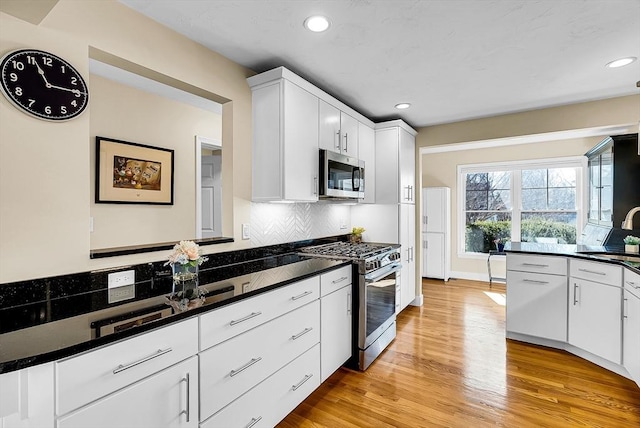 kitchen with light wood-type flooring, appliances with stainless steel finishes, dark countertops, and tasteful backsplash